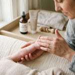 Delikatne dłonie dorosłego nakładające krem na ramię dziecka, z kosmetykami dla niemowląt w tle.